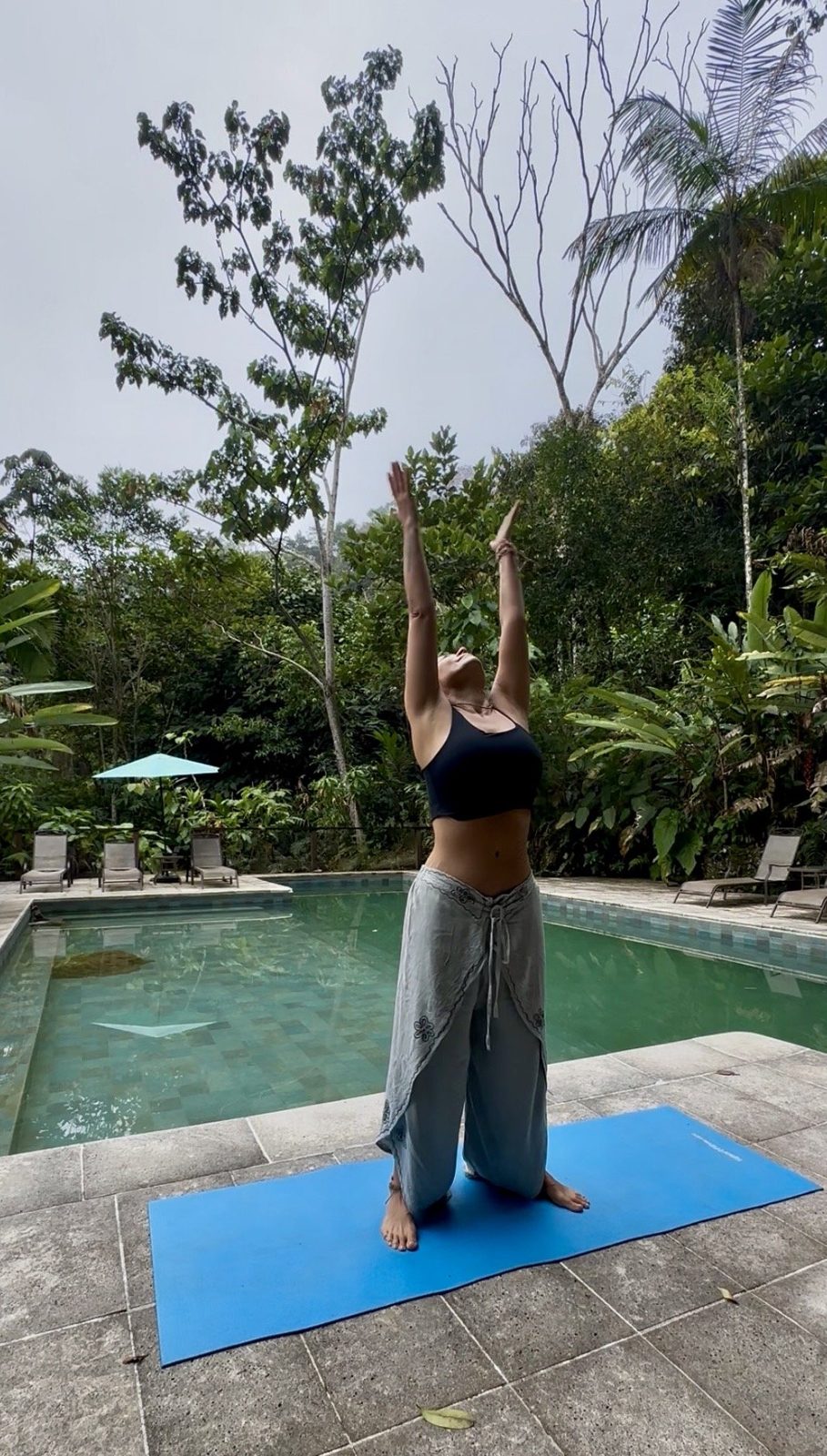 Olga con los brazos elevados al cielo sobre un tapete de yoga, rodeada de selva