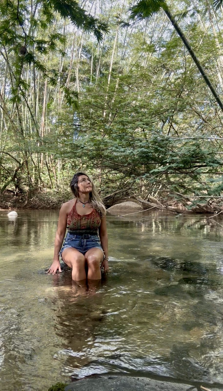 Olga sentada en un río entre bambú, mirando hacia arriba con serenidad