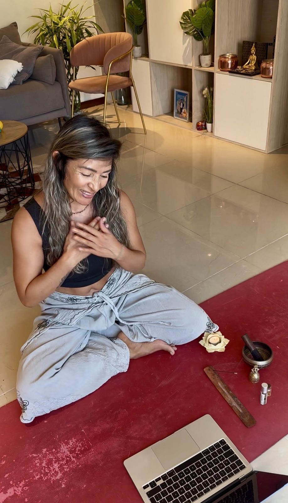 Olga guiando una sesión online con las manos en el corazón, junto a una vela y un cuenco tibetano