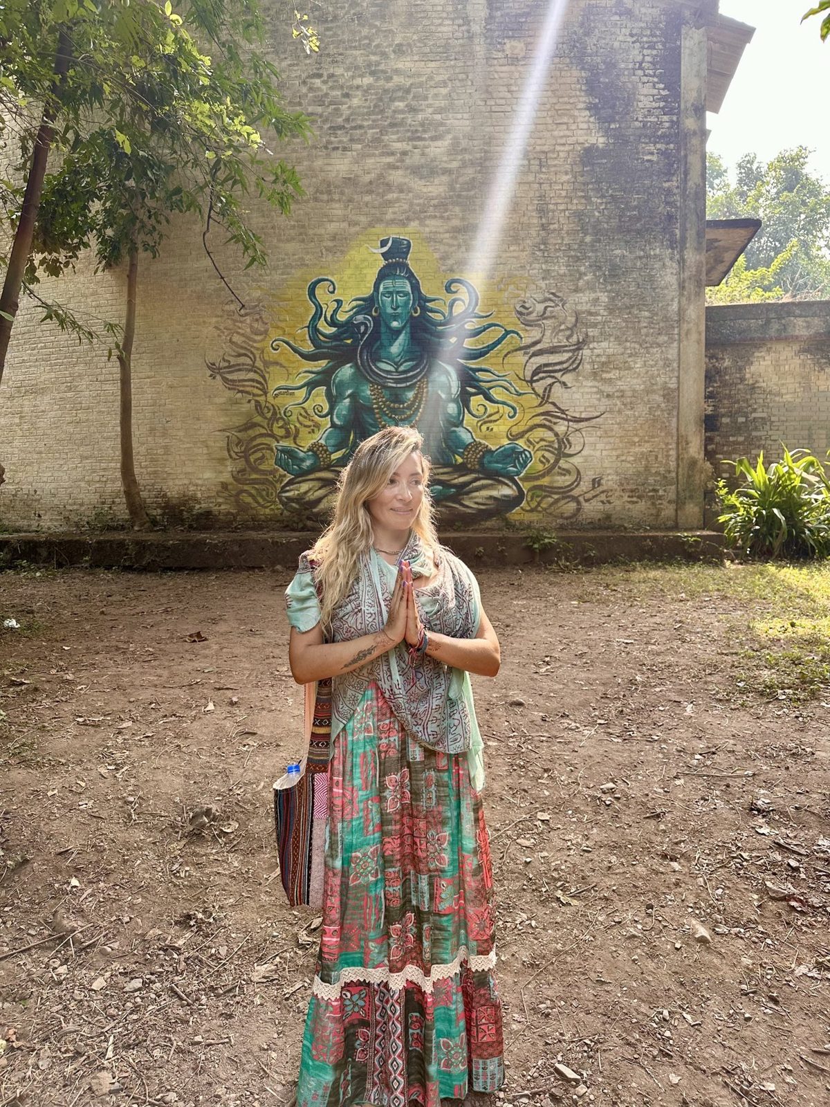 Olga con las manos unidas frente a un mural de Shiva, bajo un rayo de luz